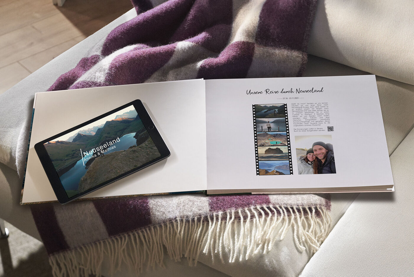 Offenes CEWE FOTOBUCH auf einem Tisch, daneben ein Tablet mit Landschaftsbild von Norwegen, gemütliche Atmosphäre mit Decke.