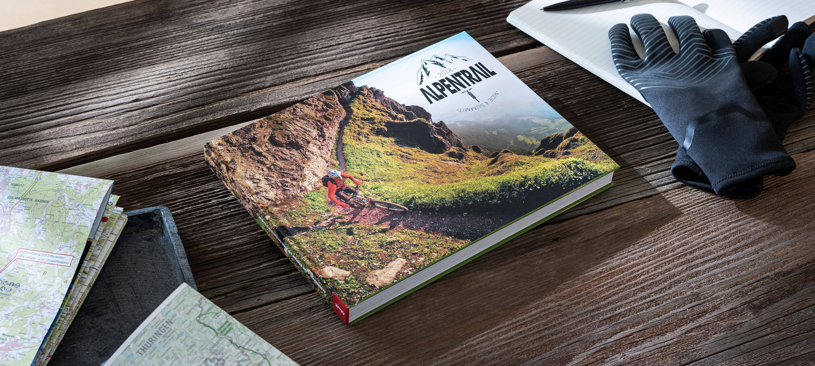 Auf einem Tisch liegt ein Fotobuch. Der Titel lautet “Alpentrail 2018”.