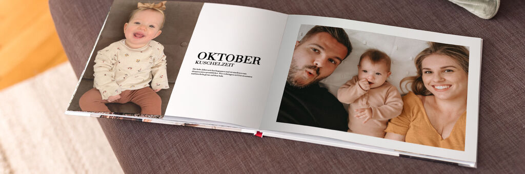 Ein aufgeschlagenes Fotobuch liegt auf einem braunen Sofa. Auf der linken Doppelseite steht "Oktober".