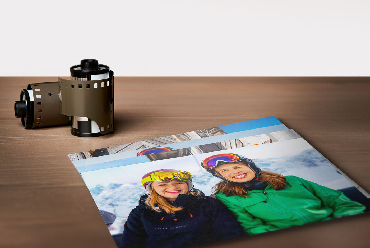 Zwei fröhliche Skifahrerinnen lächeln auf einem Foto mit Filmrollen im Hintergrund.