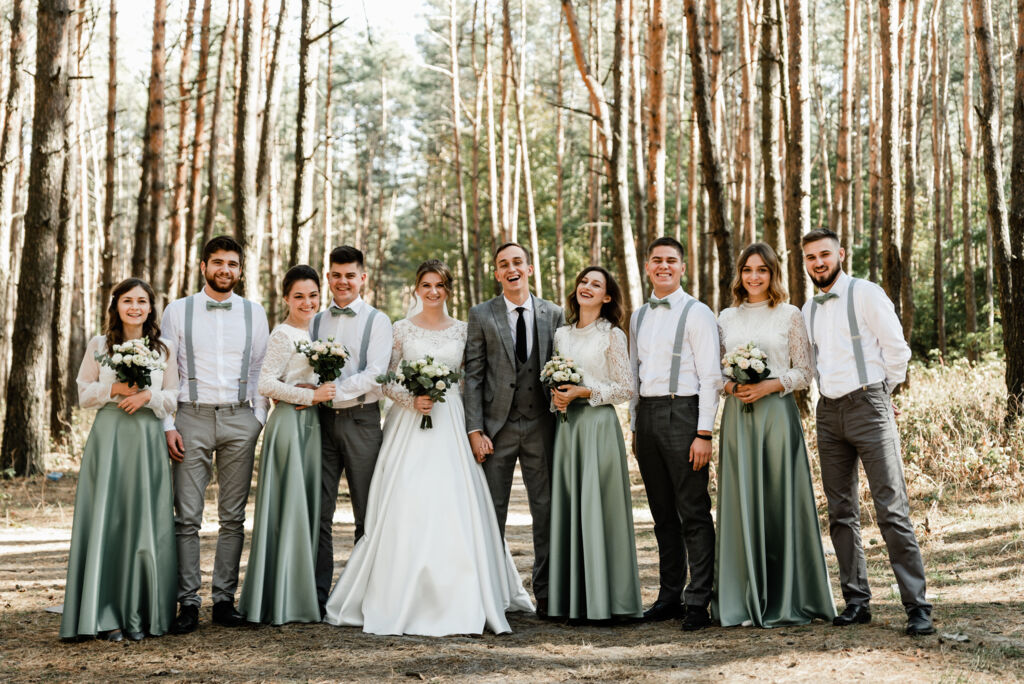 Hochzeitspaar mit acht Begleitpersonen und Blumensträußen im sonnigen Wald.