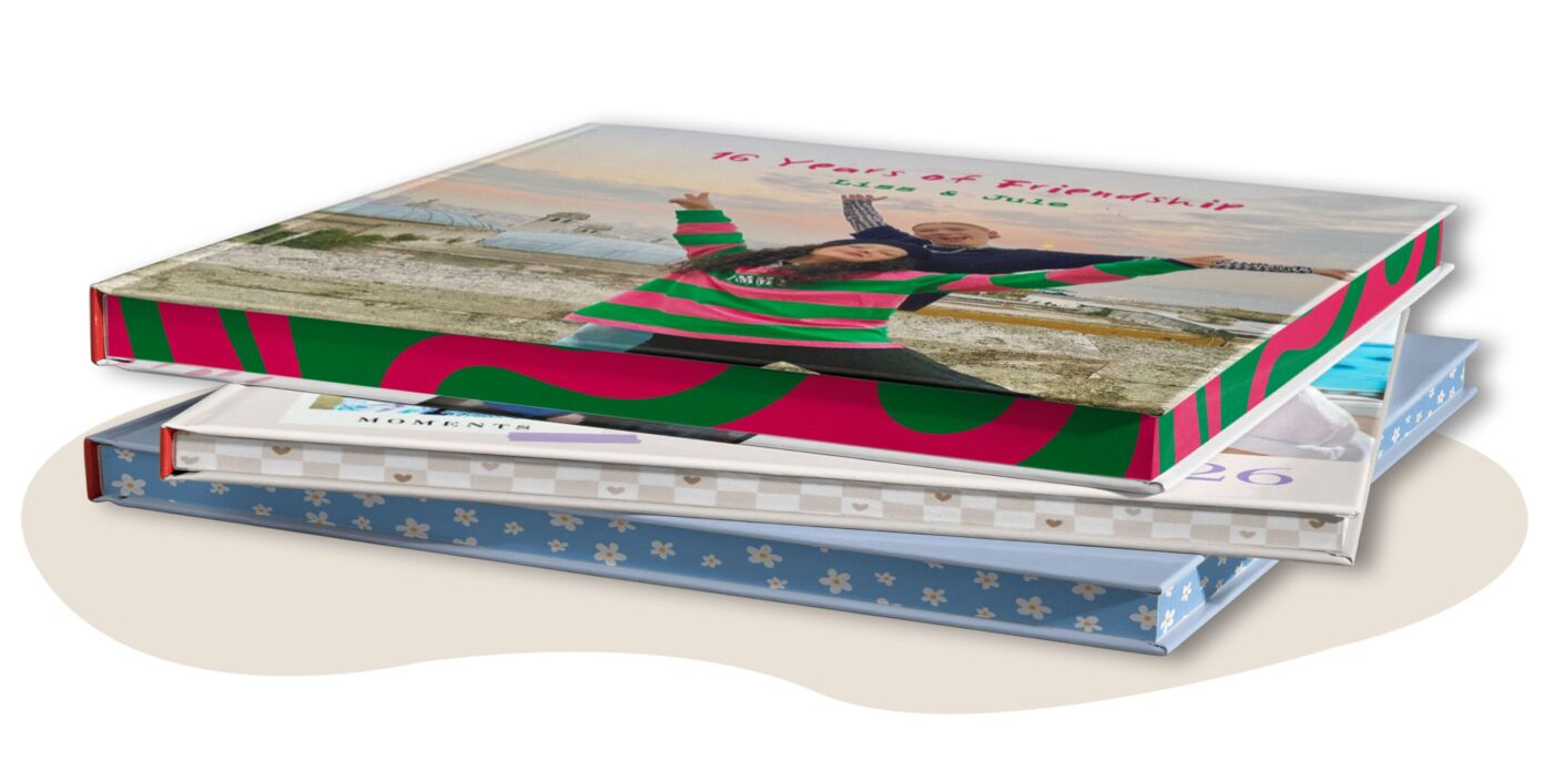 Drei gestapelte CEWE FOTOBÜCHER mit unterschiedlichen, bunten Farbschnitten und persönlichen Fotos auf den Einbänden