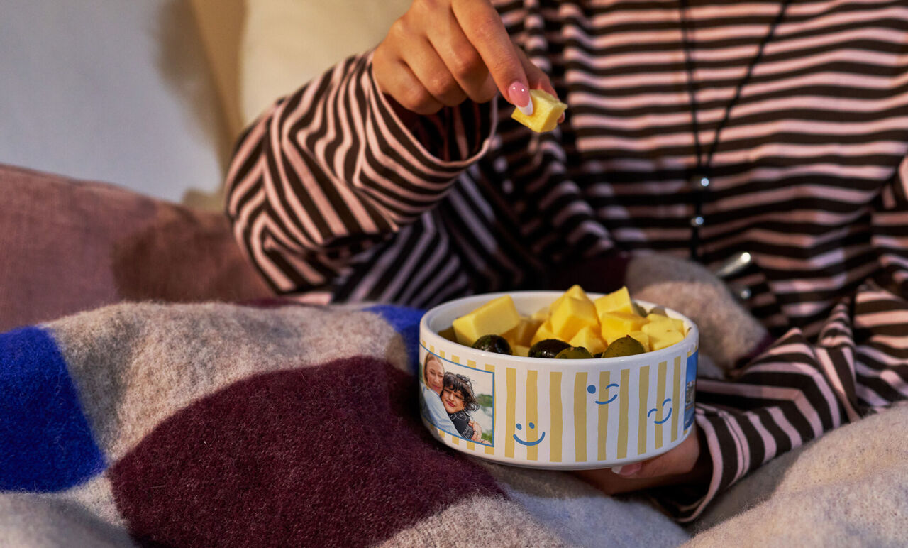 Eine Person mit gestreiftem Pullover genießt Snacks aus einer persönlichen Foto-Snackschale.