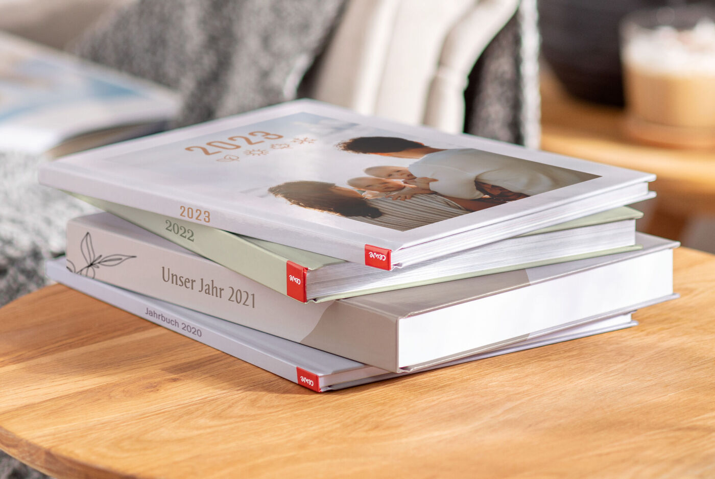Stapel aus CEWE FOTOBÜCHERN mit Familienfotos und Jahreszahlen auf einem Holztisch.