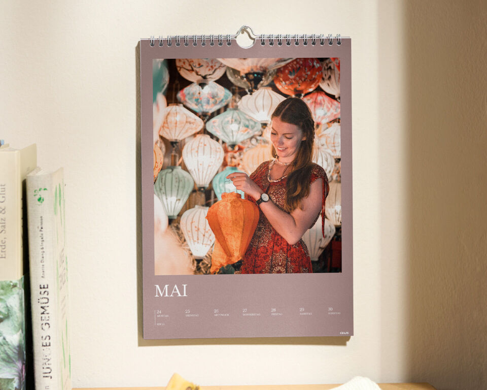 Ein CEWE Fotokalender hängt in einer gemütlichen Küche an der Wand, während eine Person lächelt.