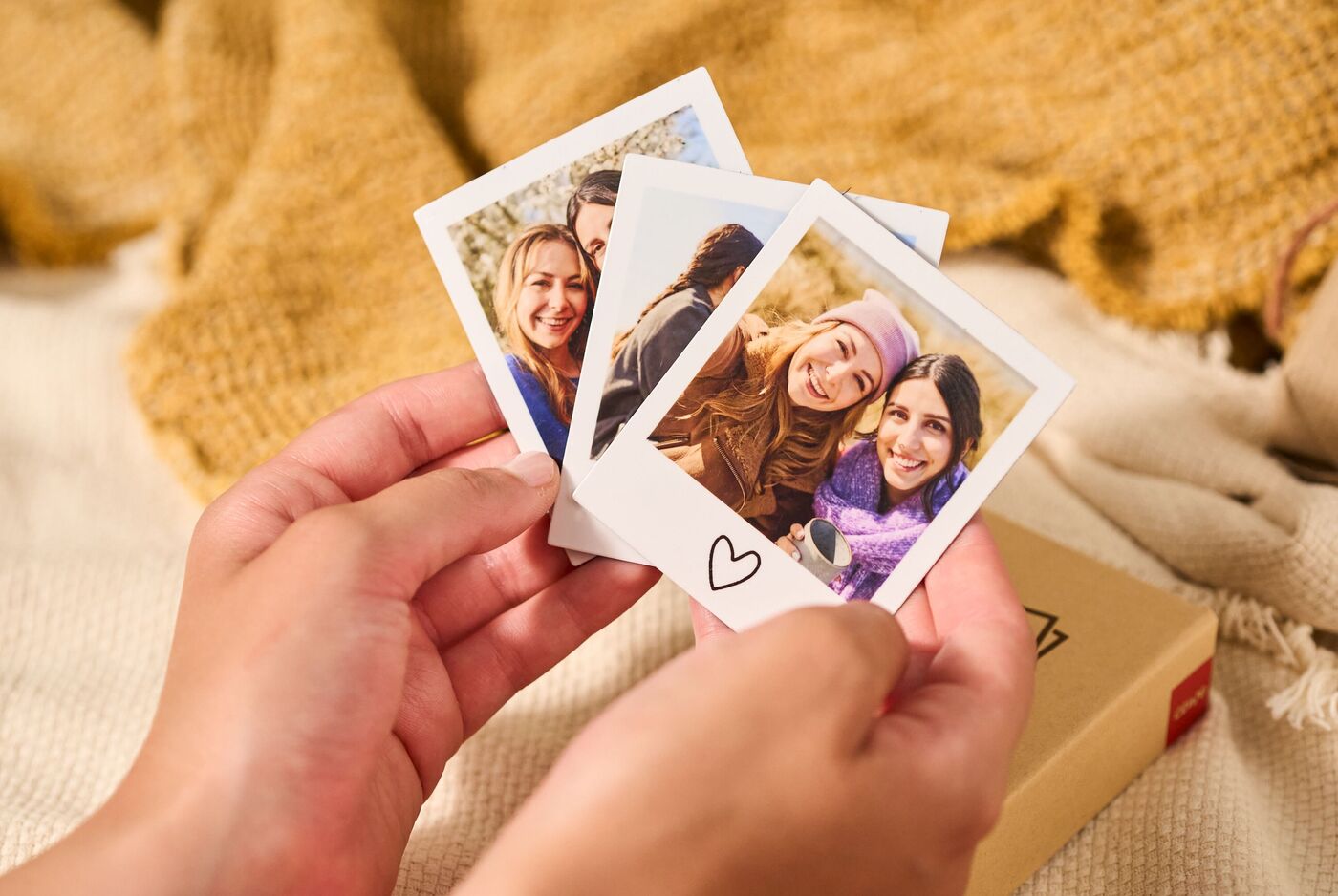Zwei Hände halten drei Fotoabzüge im Retro-Stil mit weißem Rahmen, die freundschaftliche Momente zeigen