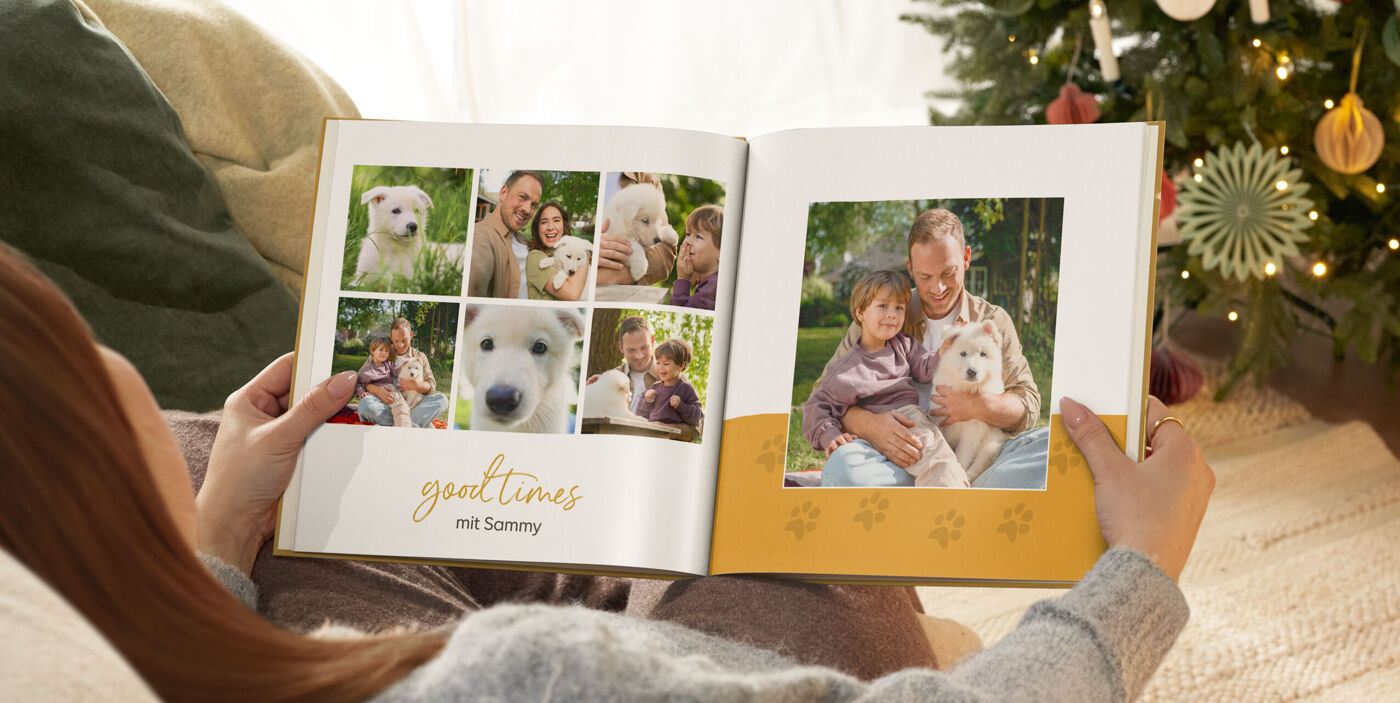 Person betrachtet ein CEWE FOTOBUCH mit Familien- und Hundefotos in weihnachtlicher Umgebung.