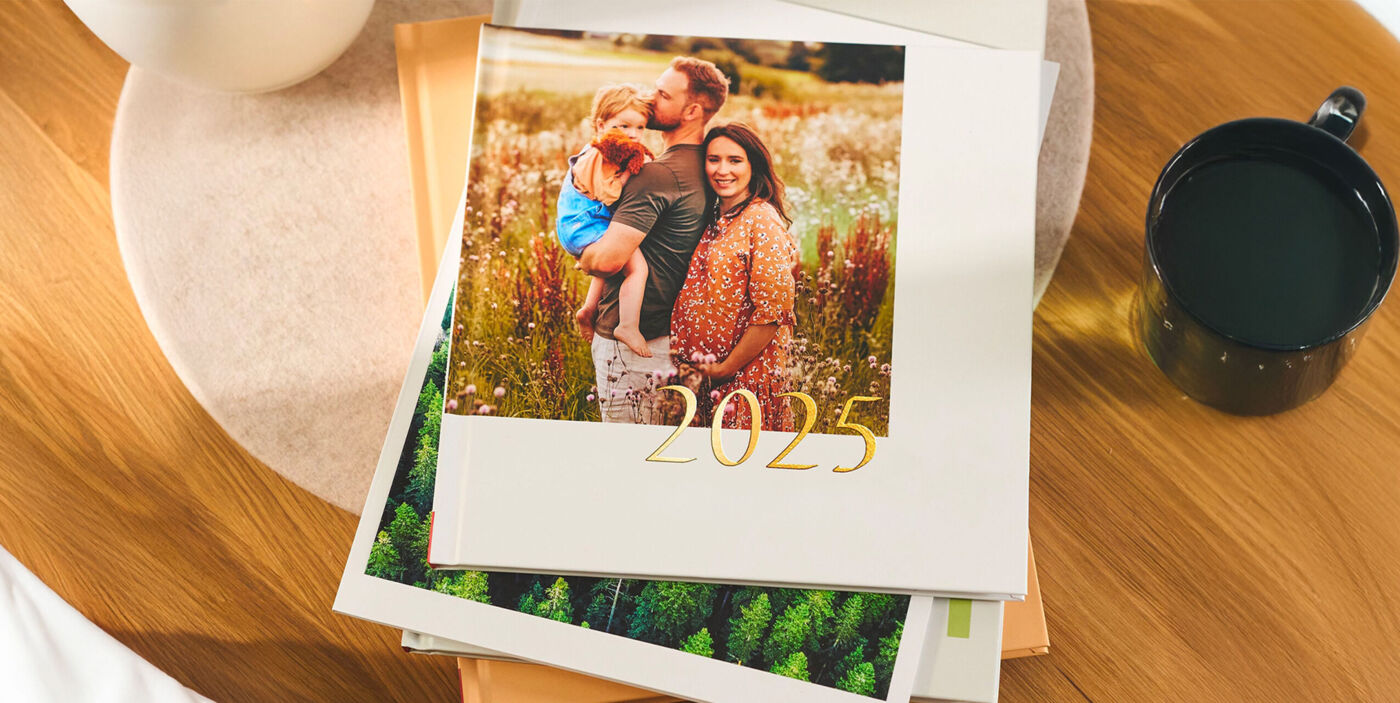 CEWE FOTOBUCH mit Familienfoto und dem Schriftzug "2025" mit Goldveredelung auf einem Bücherstapel