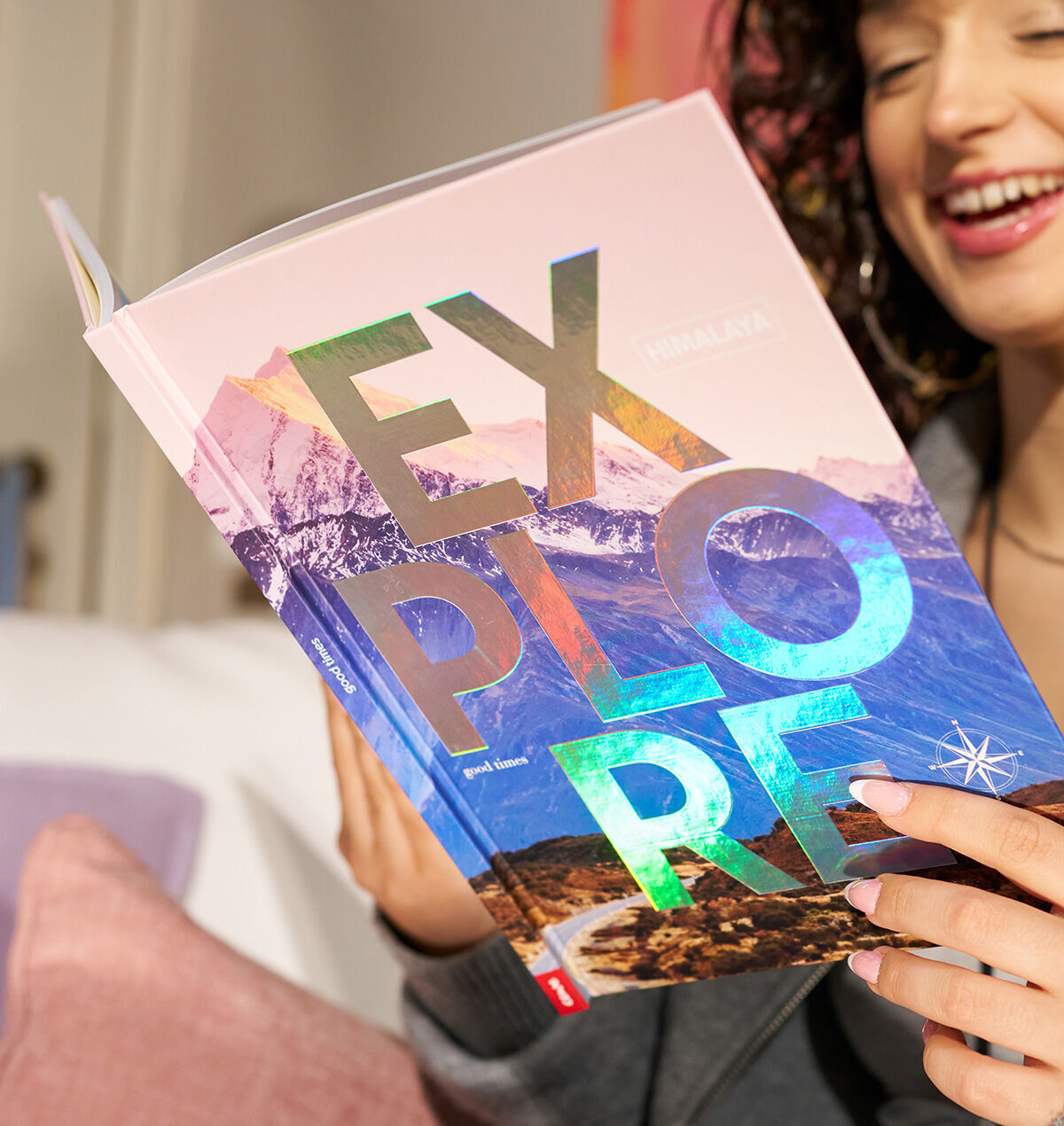 Eine Person lächelt und hält ein Buch mit dem Titel „EXPLORE“ und einer schimmernden Veredelung.
