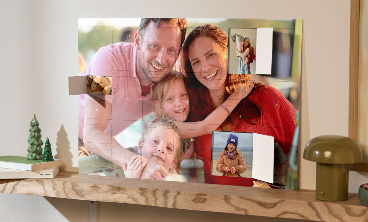 XXL Foto-Adventskalender mit Poster-Collage, bedruckt mit Familienfotos, steht auf einem Holzregal neben einer Lampe und Weihnachtsdeko