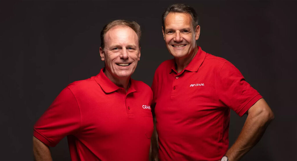 Zwei lächelnde Personen in roten Poloshirts stehen gemeinsam vor einem dunklen Hintergrund.
