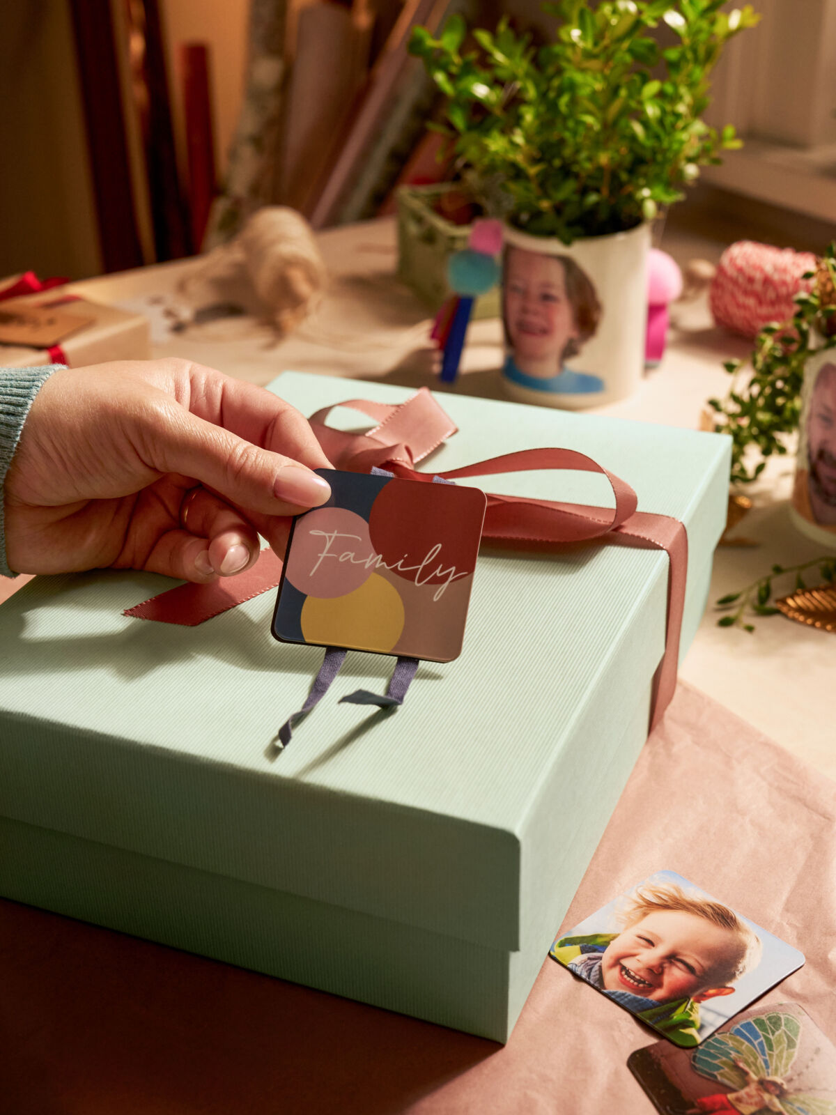 Eine Person befestigt zwei Magneten mit dem Schriftzug „Family“ als Anhänger an einem Geschenk.