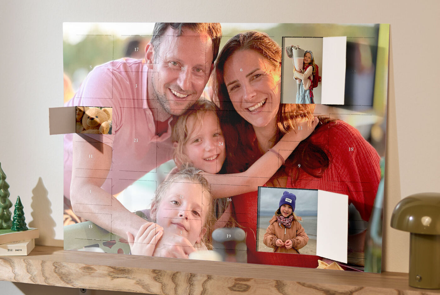 XXL Foto-Adventskalender mit Poster-Collage, bedruckt mit Familienfotos, steht auf einem Holzregal neben einer Lampe und Weihnachtsdeko