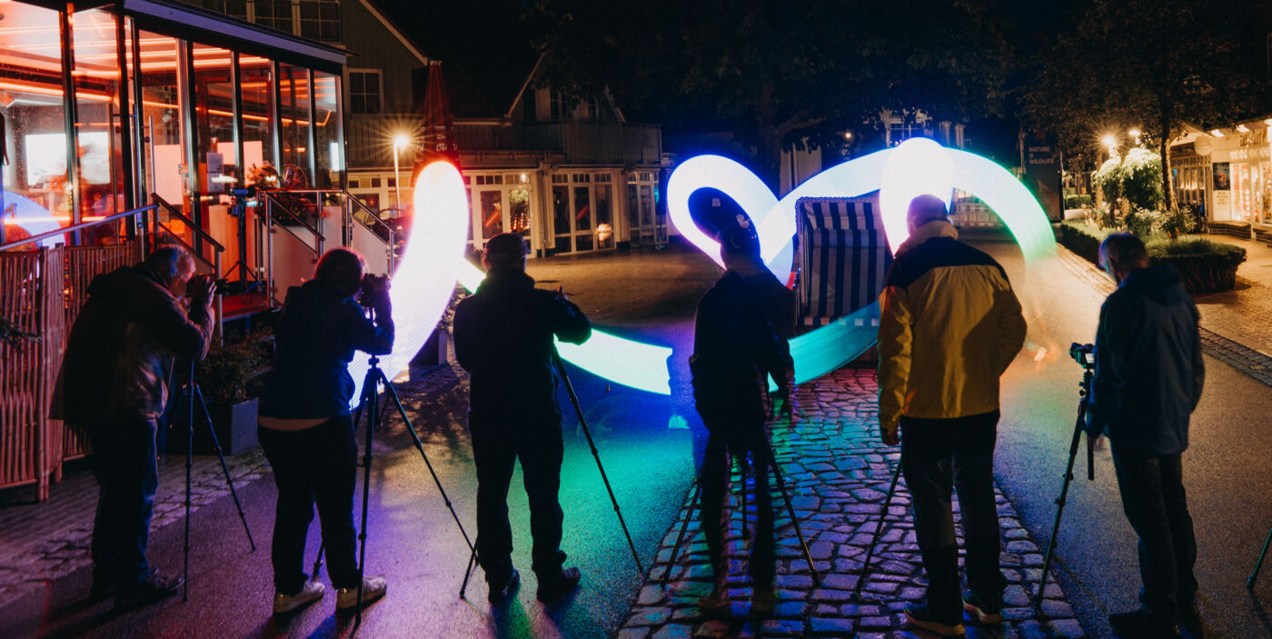 Sechs Personen stehen im Dunkeln vor ihren Kamerastativen und fotografieren einen leuchtenden Lichtschweif.