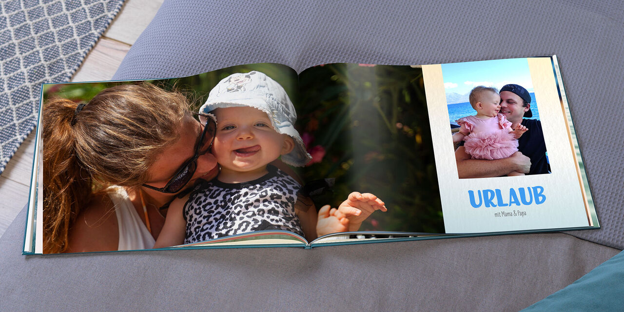 Ein aufgeschlagenes CEWE FOTOBUCH zeigt ein großes Bild von Magy und Hannah. Auf der rechten Seite ist ein kleineres Foto von Ryan und Hannah zu sehen. Darunter steht "URLAUB mit Mama und Papa".