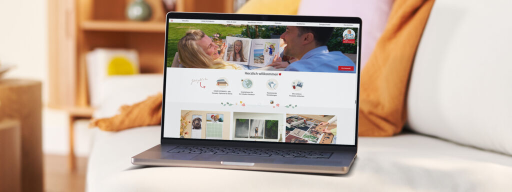 Ein Laptop zeigt die herzlich gestaltete CEWE-Webseite mit fröhlichen Menschen.