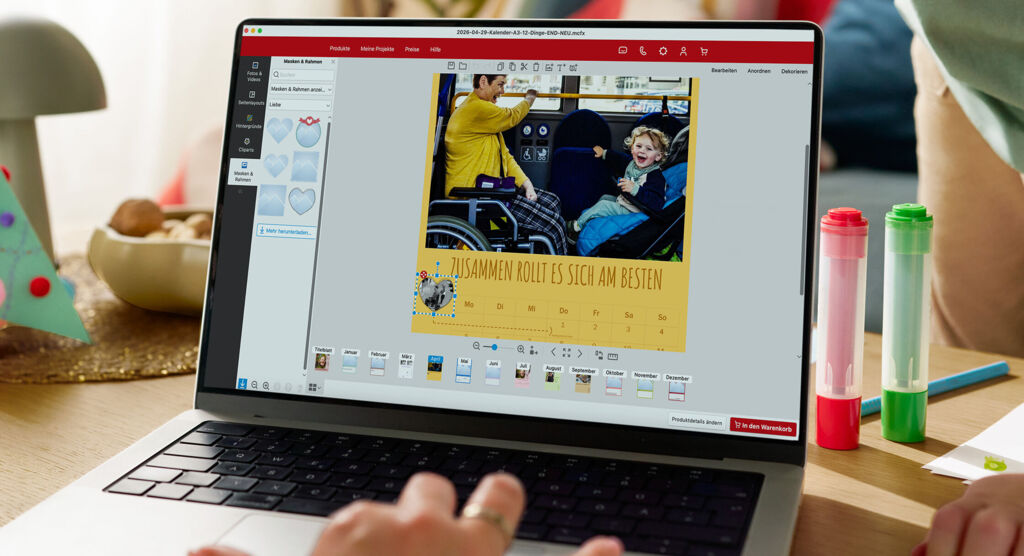 Eine Frau sitzt vor einem Laptop und gestaltet einen Fotokalender. Im Hintergrund ist ein spielendes Kind zu sehen.
