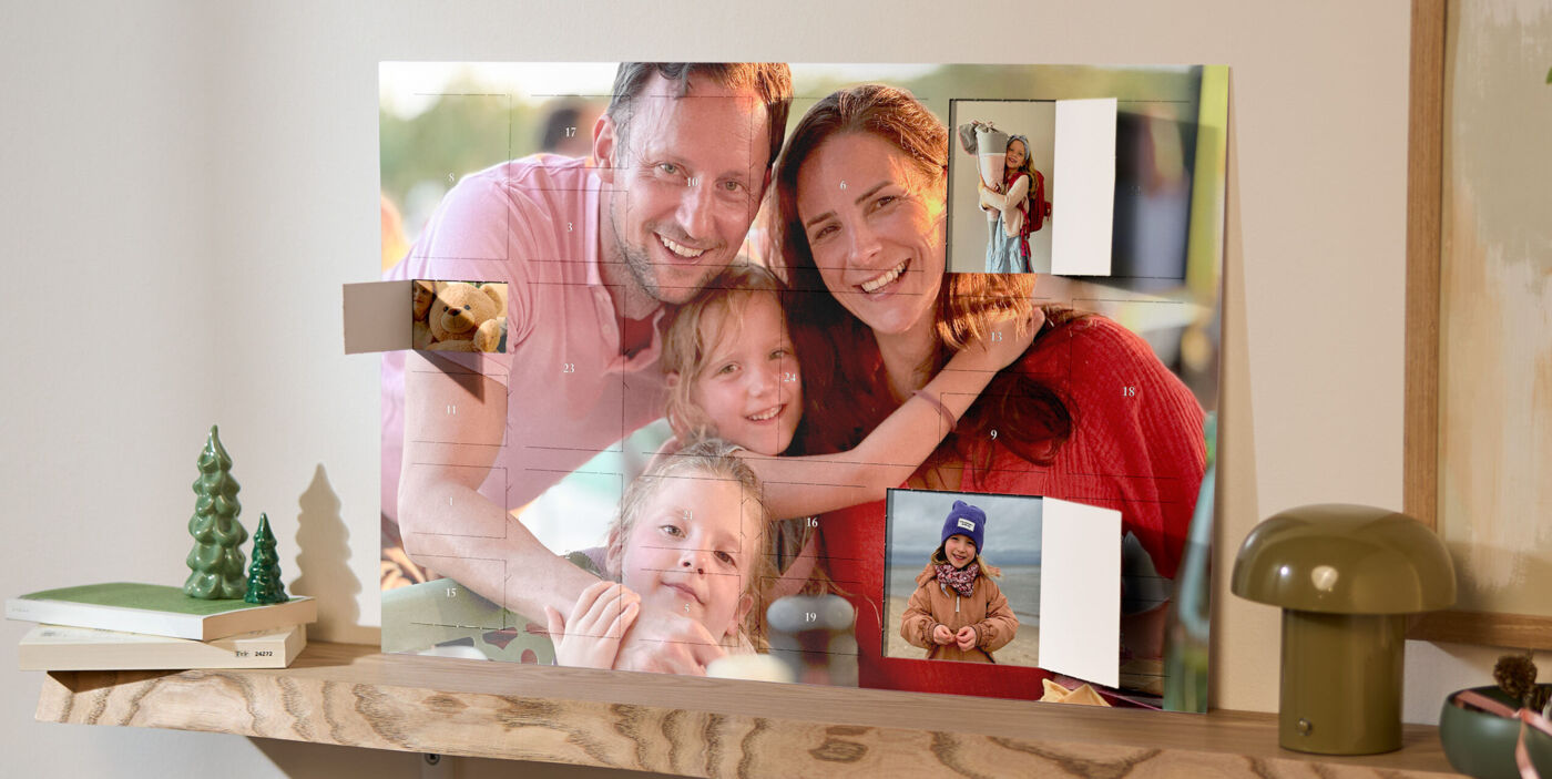 XXL Foto-Adventskalender mit Poster-Collage, bedruckt mit Familienfotos, steht auf einem Holzregal neben einer Lampe und Weihnachtsdeko