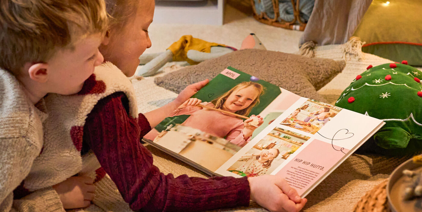 Zwei Kinder betrachten gemeinsam ein CEWE FOTOBUCH auf einer gemütlichen Decke.
