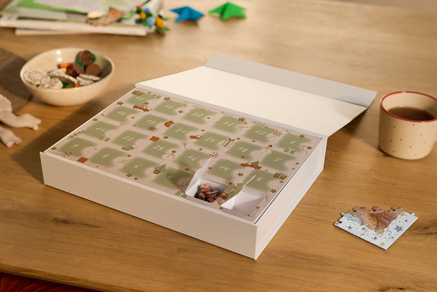 Premium Puzzle-Adventskalender mit zwei geöffneten Türchen und einem bereits gepuzzelten Puzzlestück in weihnachtlicher Umgebung