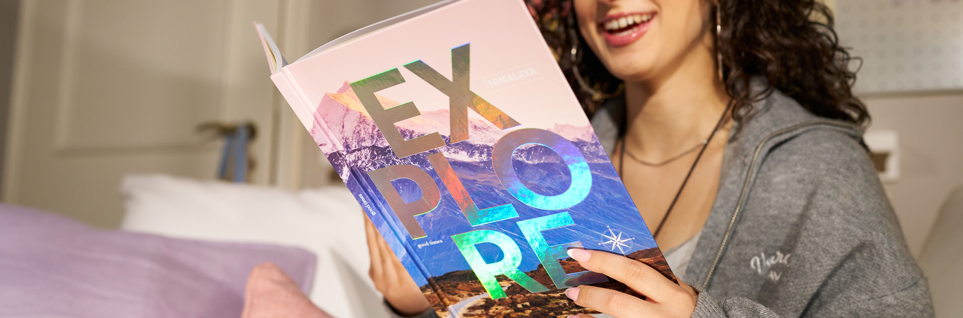 Eine Person lächelt und hält ein Buch mit dem Titel „EXPLORE“ und einer schimmernden Veredelung.
