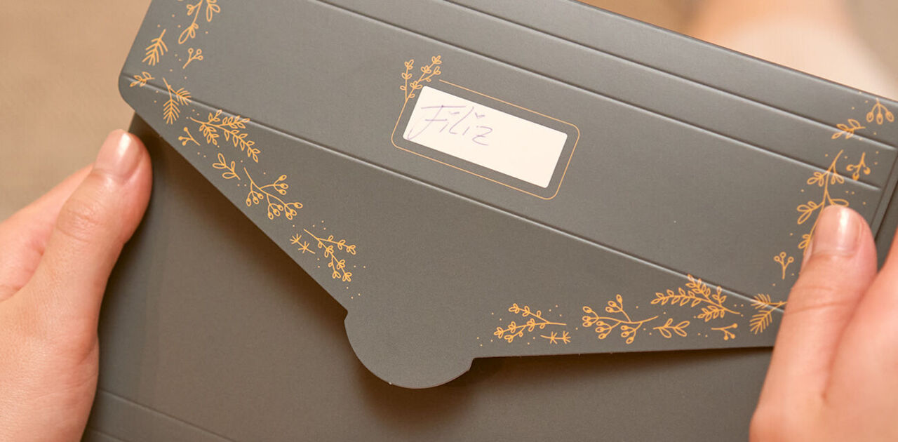 Eine grüne Geschenkverpackung mit goldenen Pflanzendetails, beschriftet mit „Liz“