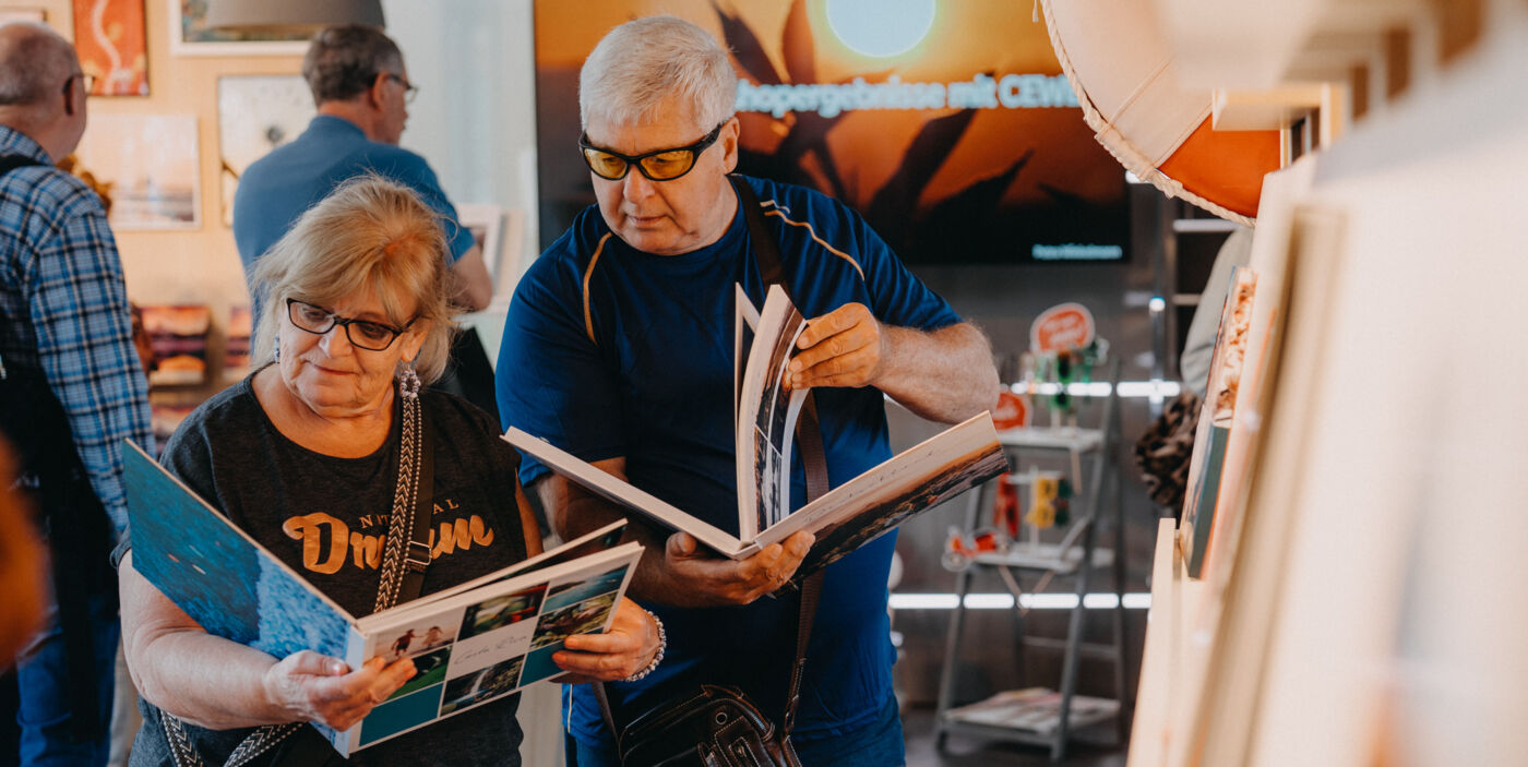Ein Mann und eine Frau stehen in einem Showroom. Jeder blättert in einem Fotobuch.