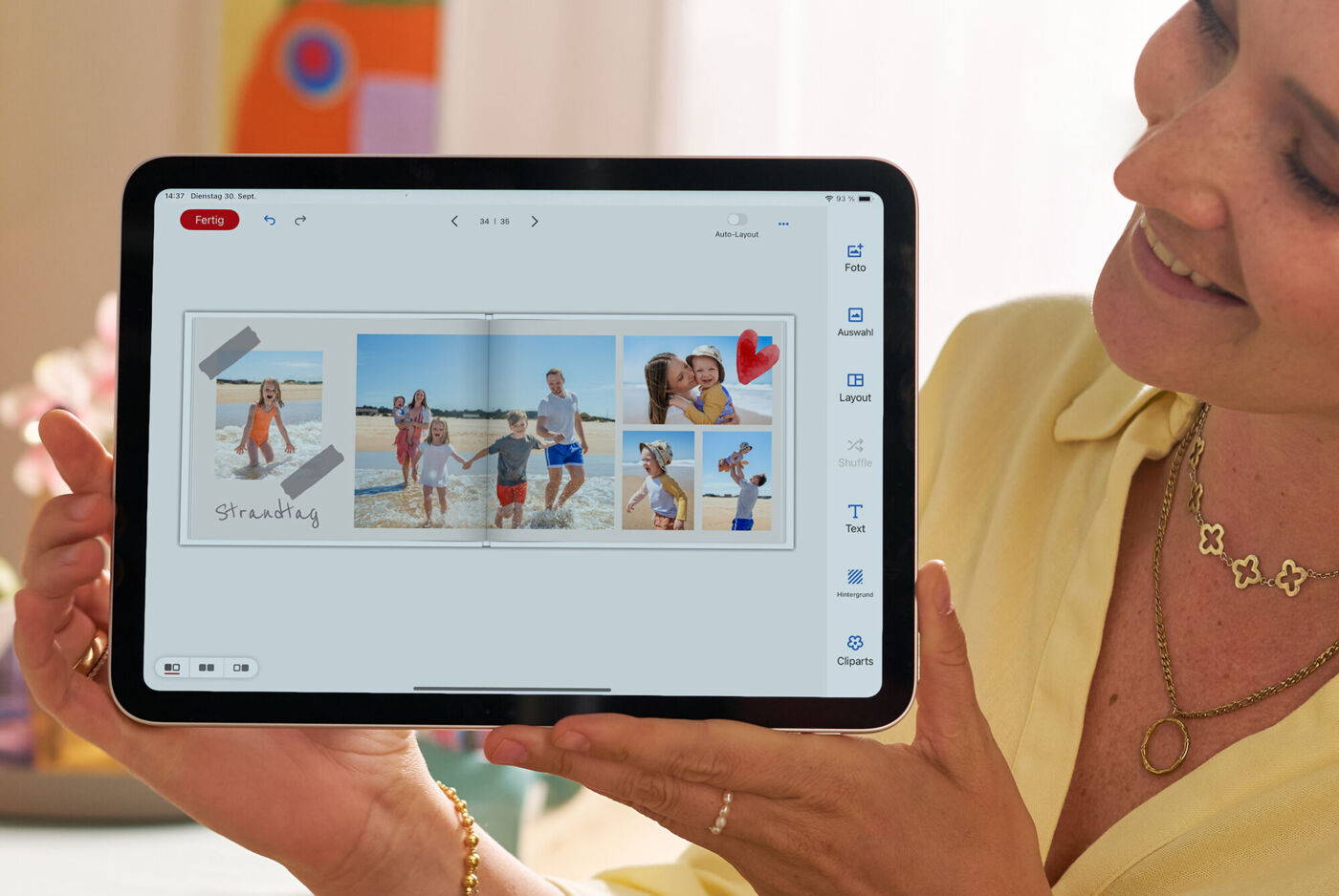 Frau hält ein Tablet mit einer gestalteten Fotoseite mit Cliparts und Urlaubsfotos am Strand.