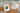 Auf einem Holztisch mit hellgrüner Tischdecke und weißen Bändern liegen zwei Hochzeitseinladungen als Klappkarten. Die linke Variante hat ein Bild der Verlobten, die rechte kommt ohne Foto nur mit Text und Cliparts aus.