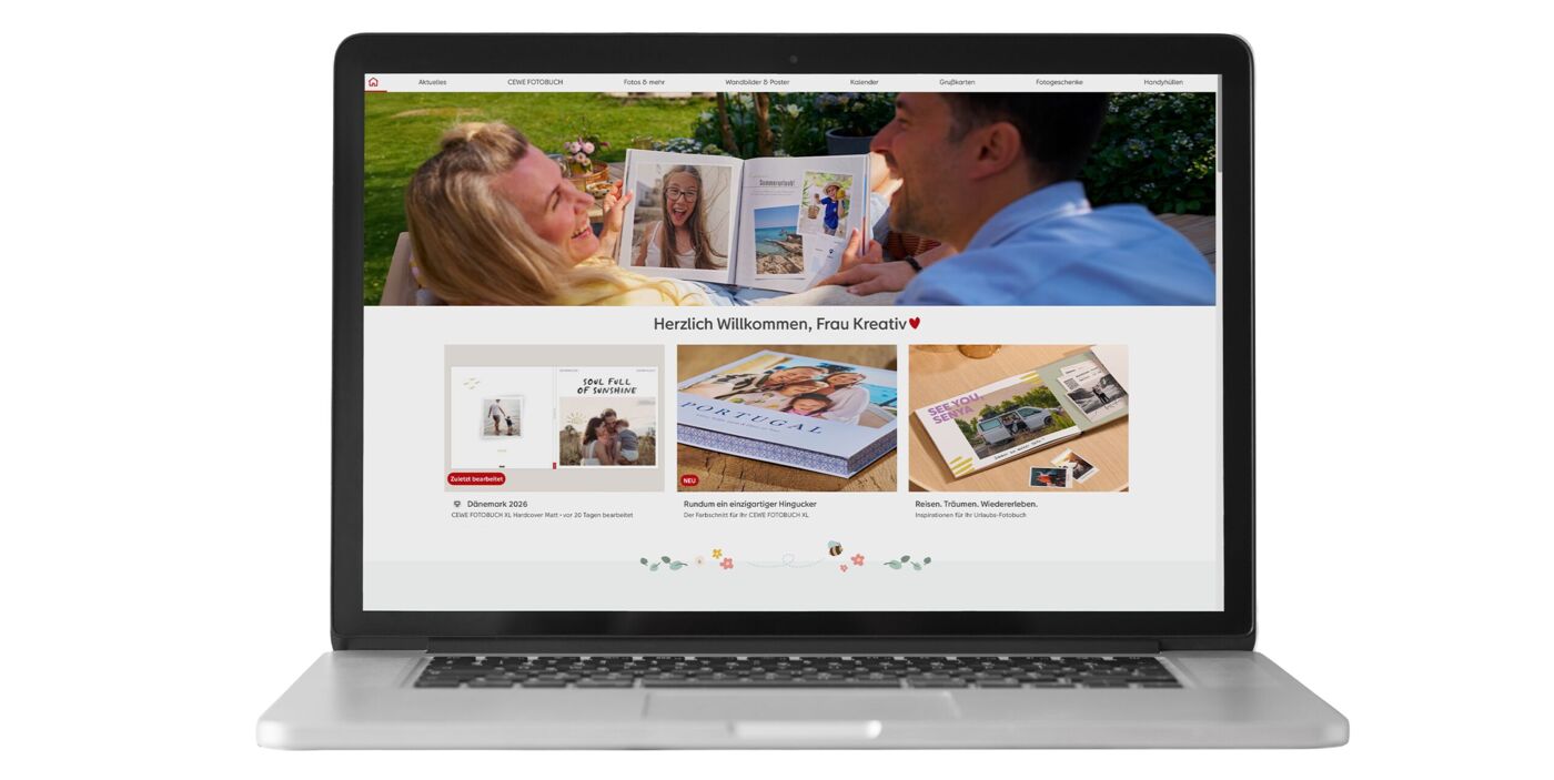 Zwei Personen schauen lächelnd auf ein CEWE FOTOBUCH auf einem Laptop.