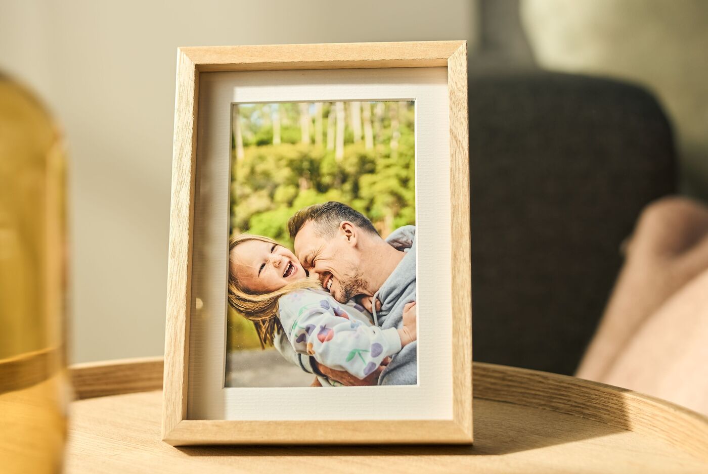 In einem hellen Raum steht auf einem runden Holztisch ein aufrecht platzierter Holz-Bilderrahmen mit einem fröhlichen Foto