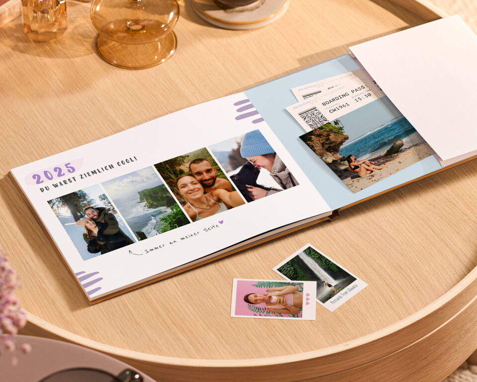 Ein CEWE FOTOBUCH liegt offen auf einem Tisch, umgeben von Erinnerungsfotos und Tickets.