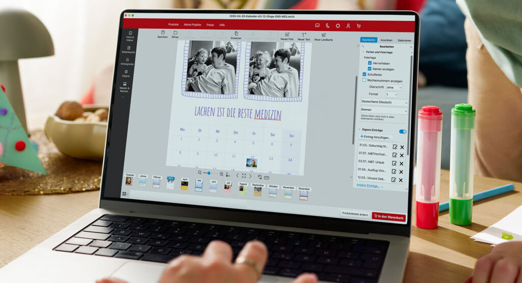 Eine Frau sitzt vor einem Laptop und gestaltet einen Fotokalender. Im Hintergrund ist ein spielendes Kind zu sehen.