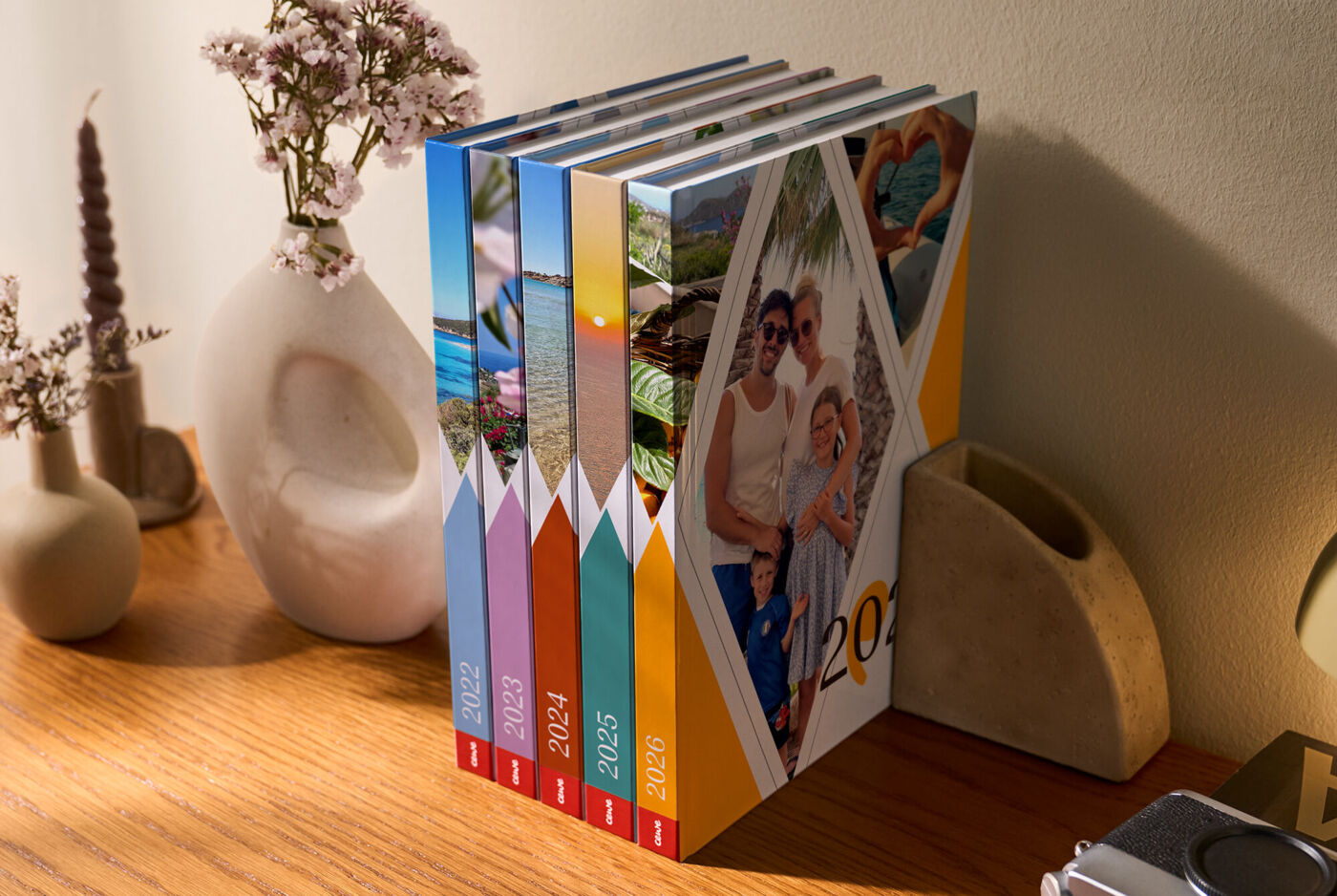 Mehrere bunte Bücher im einheitlichen Einband stehen aufrecht auf einem Holzregal neben dekorativen Vasen