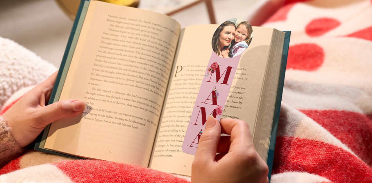Eine Hand hält ein aufgeschlagenes Buch mit einem personalisierten Lesezeichen für Mütter.
