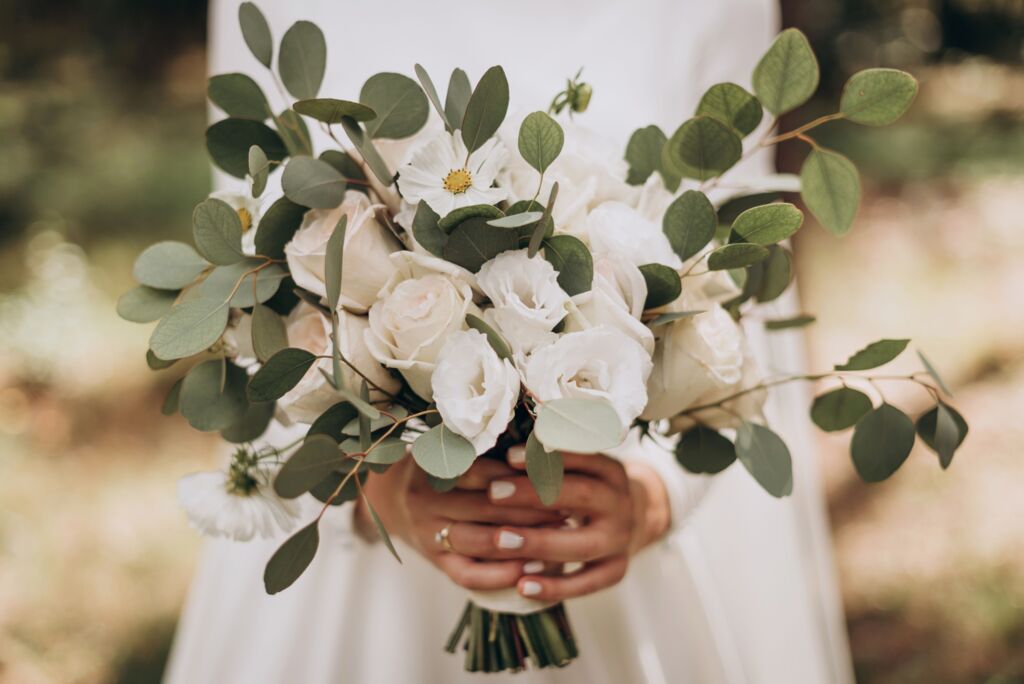 Frau in weißem Kleid hält einen Strauß aus weißen Blumen und grünen Blättern.