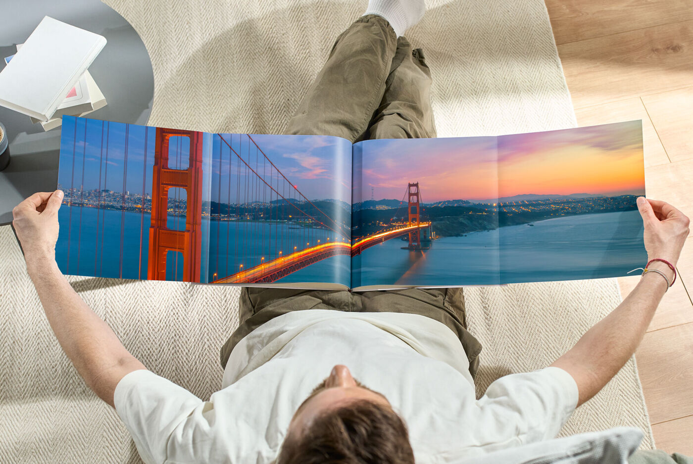 Ein Mann liegt auf dem Boden und betrachtet ein geöffnetes CEWE Fotobuch mit einem Bild der Golden Gate Bridge im Sonnenuntergang.