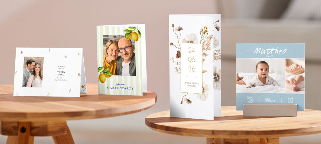 Vier Grußkarten mit verschiedenen Designs und Anlässen stehen auf zwei runden Holztischen.