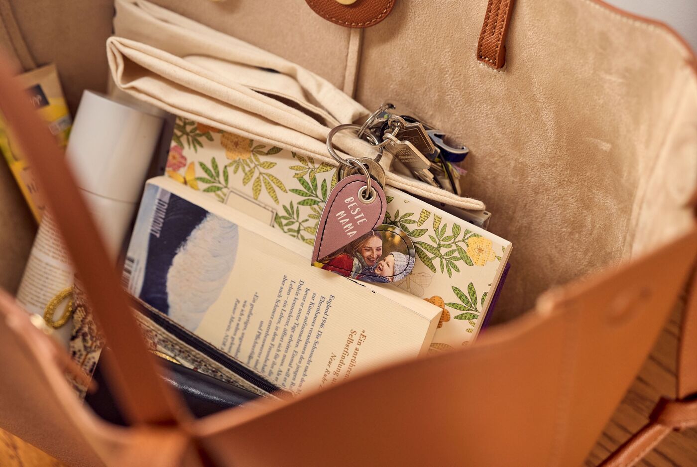 Eine offene braune Handtasche mit mehreren Gegenständen wie einem Buch, einem Notizheft und einem Schlüsselbund