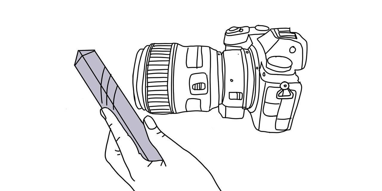 Eine gezeichnete Kamera ist zu sehen. Eine gezeichnete Hand hält ein Prisma vor die Linse.