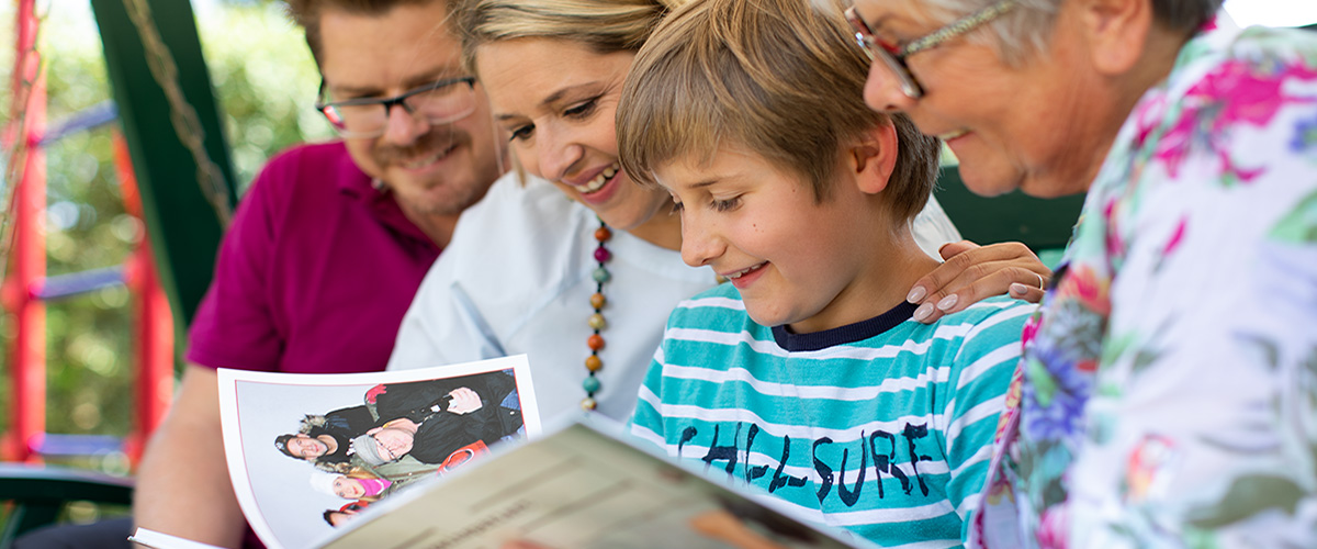 Marcus, Hannah und Jacob Fischer schauen sich mit Uschi Fischer ein CEWE&nbsp;FOTOBUCH an.