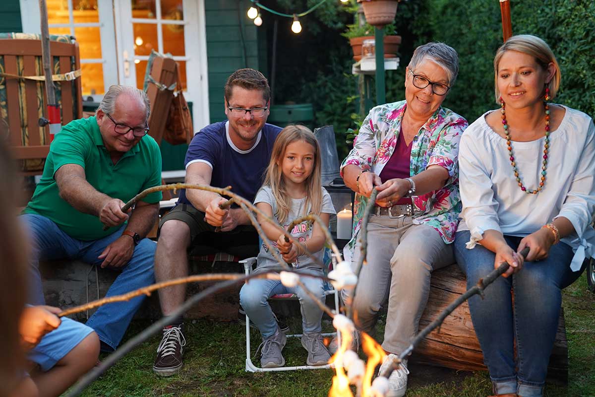 Familie Fischer sitzt gemeinsam am Lagerfeuer und röstet Marshmellows.