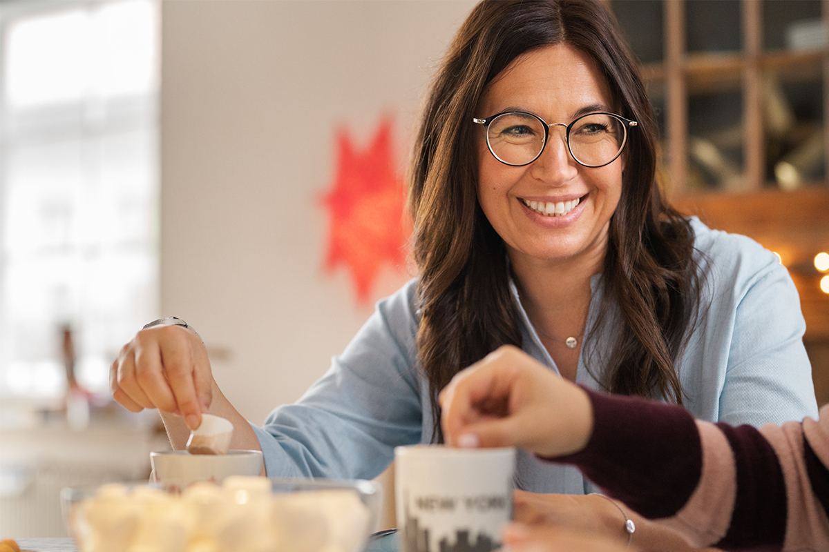 Jana sitzt am Tisch und tunkt einen Marshmallow in ihren Kakao.