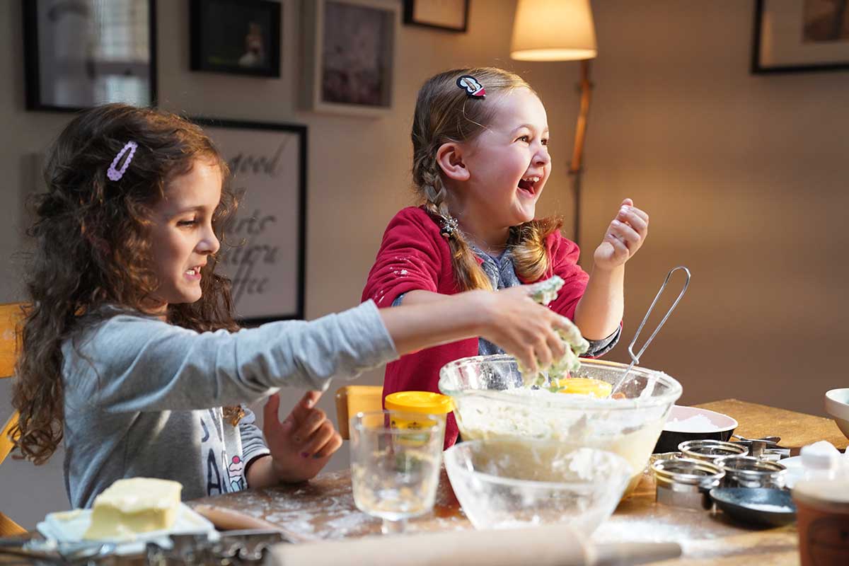 Hanna und Mathilda backen gemeinsam Kekse und lachen dabei.