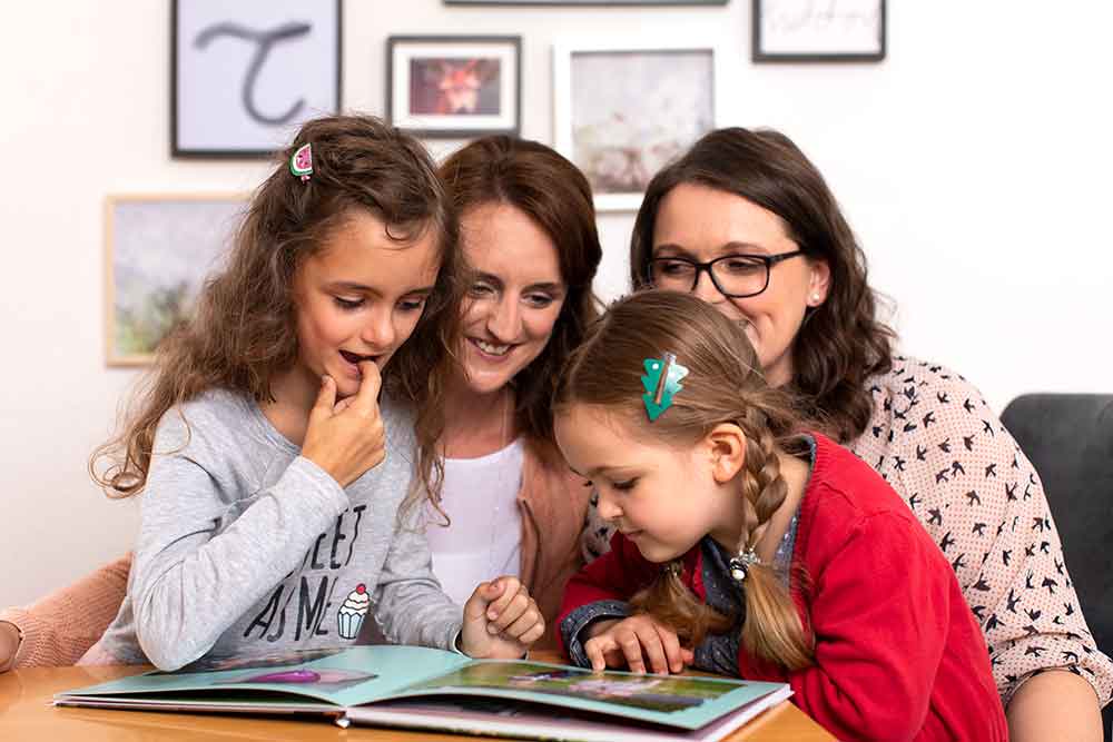 Tina Kneitz und Tochter Hanna blättern mit Melanie Kofler und deren Tochter Mathilda durch ein CEWE&nbsp;FOTOBUCH.