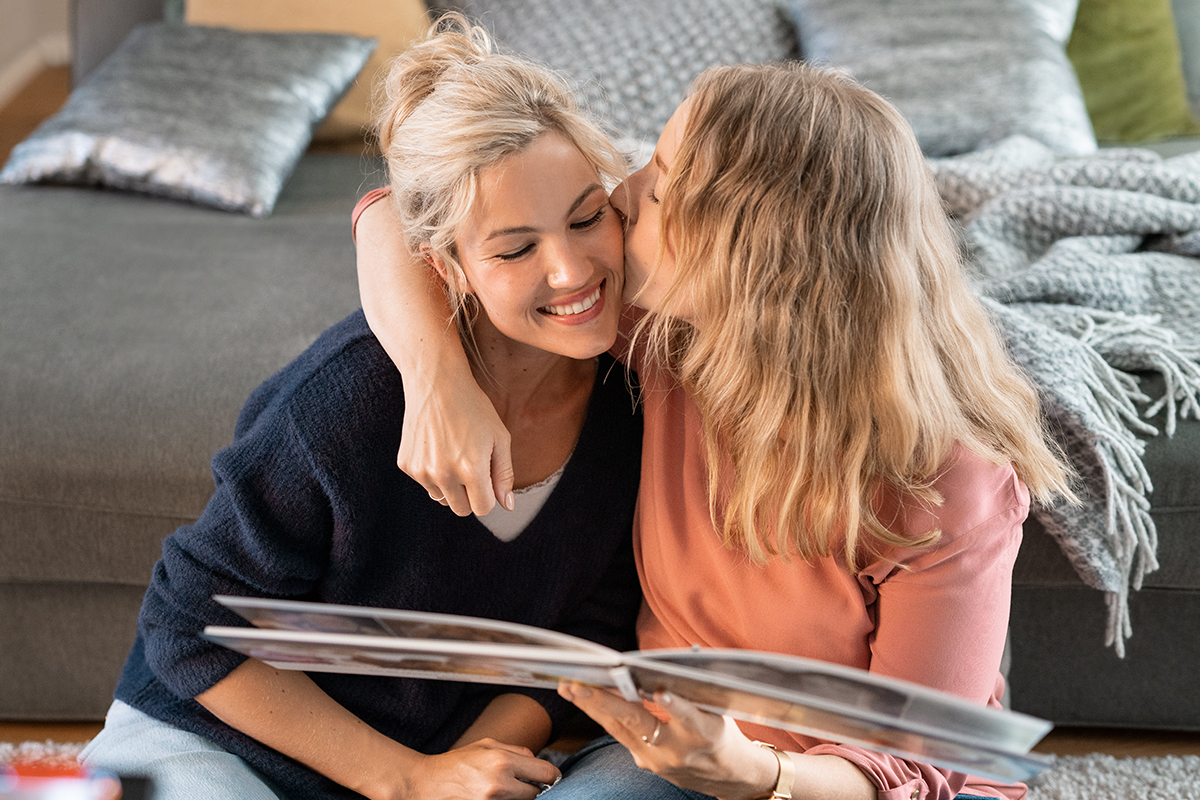 Carina hält das Fotobuch in Händen und gibt Mareike einen Kuss auf die Wange.
