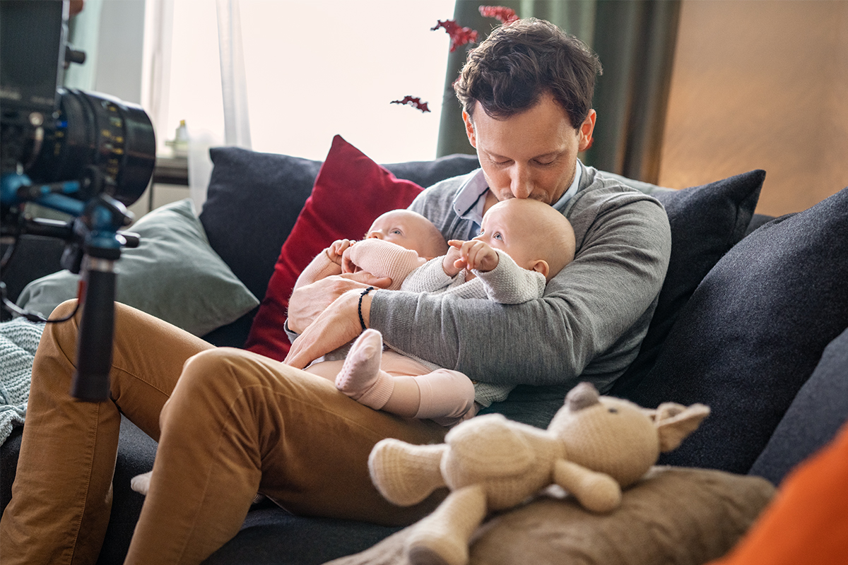 Tim sitzt auf dem Sofa und hält die Zwillinge im Arm.