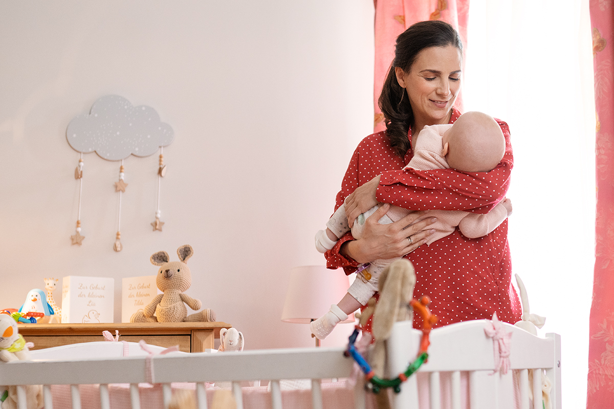 Nadine hält eins der Babys im Arm und steht vor dem Kinderbett.