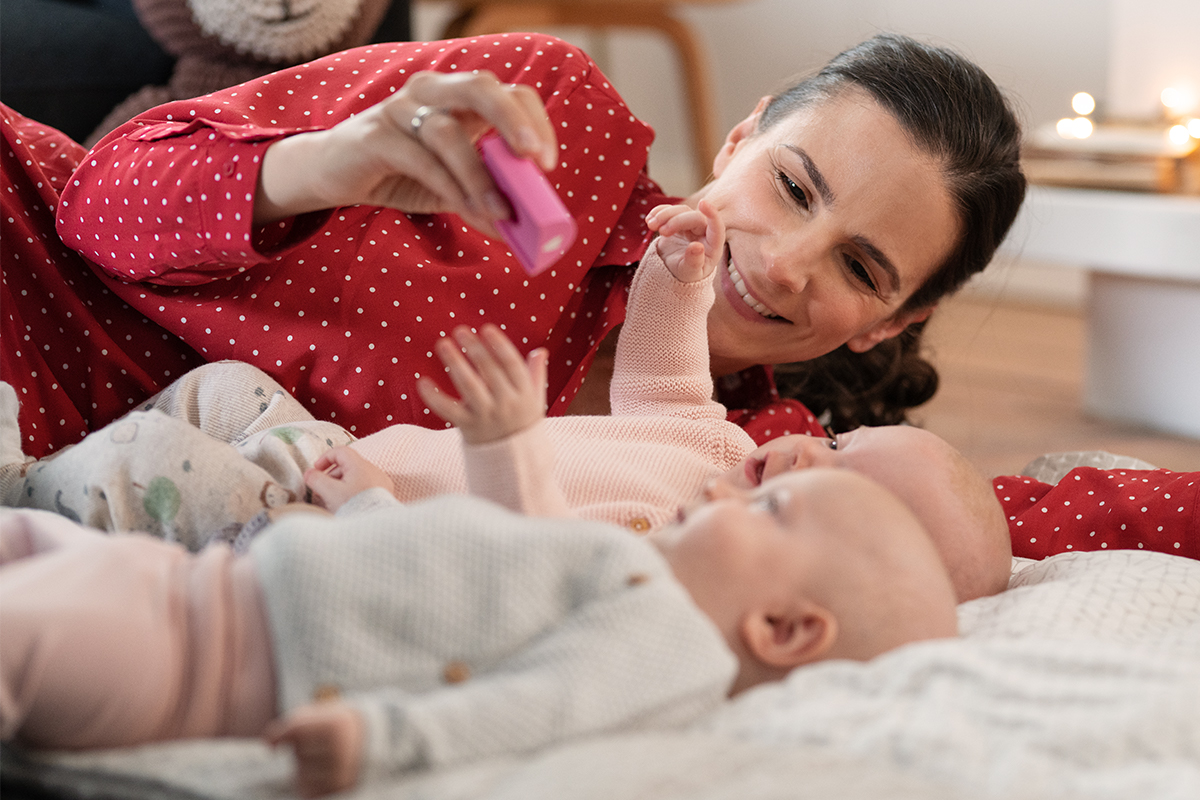 Nadine liegt neben Lia und Tilda und hält ein Spielzeug über sie.