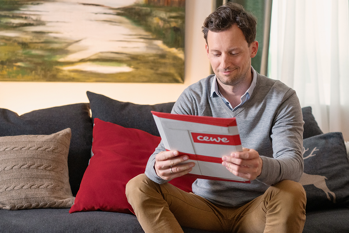 Tim sitzt auf dem Sofa und hält ein Paket von CEWE in den Händen.